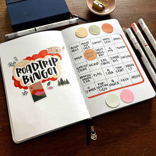 Open notebook with roadtrip bingo spread and various stationery